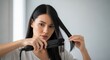 © Elenba - Portrait of young woman using hair iron for hair styling at home. Hair styling routine for beautiful long black hair, holding straightener in hands to curl or straighten her strands.
