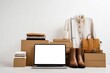 © tengah - Arrangement of folded garments, leather accessories, and a laptop against a white background, styled as a modern retail or lifestyle composition