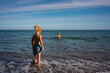 © sutulastock - Father and son spending time together at the seaside, little boy standing on the shore watching his dad swimming in the sea on a calm summer day