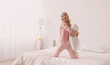 © Prostock-studio - Fun with joy, enjoying carefree leisure weekend time alone in bedroom, celebrating freedom. Glad young blonde woman in pink pajamas and sleep mask play with pillow on bed in white bedroom interior
