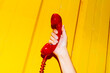 © Juan Moyano/Stocksy - man holding red telephone receiver on yellow wall