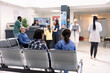 © DC Studio - Hospital staff assist patients at front desk in organized emergency waiting area. Nurse in blue scrubs consults seated asian man as other patients and doctors prepare for medical consultations.