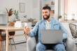 © Pixel-Shot - Young bearded man working with laptop and mobile phone in armchair at home