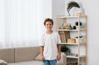 © SHOTPRIME STUDIO - Smiling boy stands indoors in a bright, minimalist living room with white shirt and jeans, creating a candid portrait with warm natural light, soft cushions, and greenery in the background.