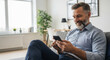 © l1gend - Smiling mature business man entrepreneur or trader using mobile phone device sitting on sofa at modern home office. Bearded handsome businessman browsing online holding mobile cellphone app. Vertical