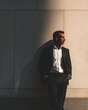 © chanchai - Elegant Man in Suit Posing by Wall: A distinguished man in a tailored suit exudes confidence and sophistication as he leans casually against a minimalist wall, bathed in the warm glow of sunlight.