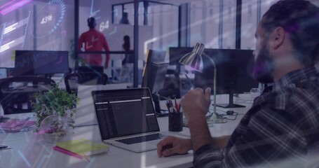 Typing bearded man working at open-plan office desk, with laptop and desk lamp, copy space
