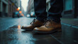 Brown leather shoes on a wet city street at dusk, reflecting ambient light from vehicles and buildings, creating a moody urban atmosphere.
