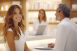 © Chatchaa - A cheerful woman smiles at the camera while a man and another woman engage in conversation in a bright, modern setting.