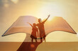 © kieferpix - Children silhouettes stand inside glowing sunset with an open book bible, symbolizing family learning, and inspiration. Hope, religious belief education and togetherness themes.