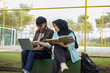 © Fajar - Two students studying outdoors, using a laptop and a book, likely collaborating or working on a project together, at a park or campus setting