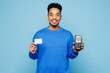 © ViDi Studio - Young man of African American ethnicity wear sweatshirt casual clothes hold wireless modern bank payment terminal to process acquire credit card isolated on plain pastel light blue background studio.