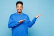 © ViDi Studio - Young man of African American ethnicity wear sweatshirt casual clothes point hands arms aside indicate on area isolated on plain pastel light blue cyan background studio portrait. Lifestyle concept.