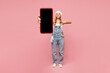 © ViDi Studio - Full body young employee handyman woman wear denim overhaul hold use blank screen mobile cell phone isolated on plain pink background. Instruments for renovation apartment room. Repair home concept.