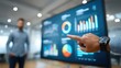 © Oulaphone - A person points at a large digital screen displaying colorful business data charts and graphs in a modern office setting.