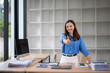 © Wasana - Smiling businesswoman showing thumbs up while standing at desk in modern office