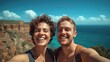 © Palmesrk - A joyful couple taking a selfie at a scenic coastal cliff with bright blue ocean and clouds