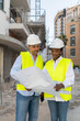 © Renata Hamuda - Construction engineer and Architect in hardhat reviewing blueprint at construction site