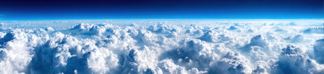 Panoramic aerial view of fluffy, billowing white clouds against a backdrop of clear, deep blue sky. A vast, serene expanse is on display