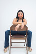 © Mdv Edwards - A fierce young Asian woman sitting on a backward chair with a strong, intense gaze that exudes confidence and power. Isolated on a white background.
