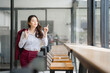 © MINAE - Young asian businesswoman standing in modern office cafeteria is holding jacket on shoulder and pointing finger at window while thinking about future projects