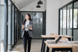 © MINAE - Young Asian businesswoman holding digital tablet walking in modern office and thinking about future projects, startup, new business, company growth, or company development