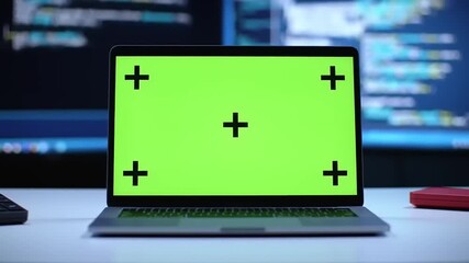 Laptop with green screen and tracking markers on a desk with code on background screens.