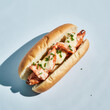 © FLGB - Lobster roll in a plain bun with butter gloss and chives on a pale blue background, three-quarter studio view with a soft grounded shadow