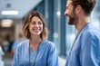 © id512 - Smiling female nurse talking with male medical colleague in hospital hallway. Friendly healthcare professionals in scrubs, concept of teamwork, care and modern medical staff