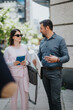 © qunica.com - Two colleagues discuss work-related materials while standing outside in a modern city environment. The interaction reflects collaboration, professionalism, and focus in a corporate context.