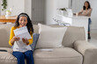 © wavebreak3 - Diverse mother and teenage daughter sitting on sofa in living area reading letter with smartphone