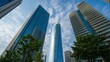© Kazi - Low angle shot of modern skyscrapers reflecting the blue sky and clouds with green trees in the foreground