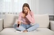 © New Africa - Emotional young woman with pregnancy test on sofa at home
