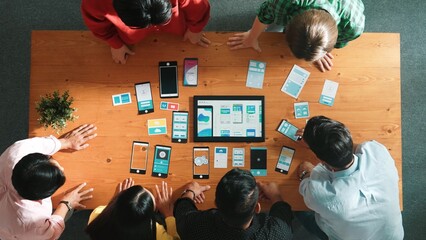 Top view of software developer team looking Ux Ui design for mobile phone interface from tablet while comparing and planning wireframe prototype designing together at creative workplace. Convocation.