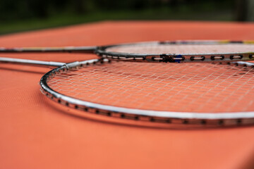 Pair of badminton rackets lying on orange surface.