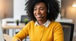 © Rohan - A smiling black woman with curly hair wearing a headset and a yellow sweater, working in an office