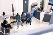 © DC Studio - Diverse people seated in waiting room, preparing for clinical consultations. Elderly man and asian guy engage in conversation as black female doctor records data of mom and daughter in hospital lobby.
