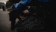 © Ruls.Design - A diligent worker in traditional attire sorts through a large pile of harvested material at a dimly lit roadside market stall