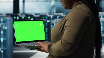 Programmer in data center using app on isolated screen laptop to ensure error free mainframes networks. Worker uses chroma key notebook to monitor server hub gear parts for failures, camera B