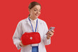 © Pixel-Shot - Female doctor with first aid kit and mobile phone on red background