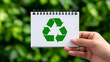 © Supot - Recycle symbol eco green sustainability concept hand card sign environment Optimistic eco message with recycle symbol white notebook held by hand, green bokeh background, clean design promotes