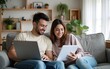 © zhao - Doing Accounting at Home: Happy Couple Using Laptop Computer, Sitting on Sofa in Apartment. Young Family Filling Tax Forms, Mortgage Documents, Bills, Checks, Balances, Invoices are in Order