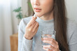 © KMPZZZ - Dietary supplement, healthy diet positive asian young woman hand holding pill capsule, take vitamin in mouth for beauty skin hair, taking medicine with glass of water at home, pharmacy and health care
