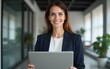 © fu - Portrait latin mature adult professional business woman looking at camera and smiling. European businesswoman CEO specialist holding digital laptop pc using fintech app standing at workplace in office