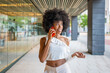 © Miquel - Young black woman talking on smartphone walking near modern building