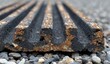 © VisualKindits - Close-up of a ridged, dark material, possibly metal or composite, resting on gravel