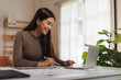 © Phimwilai - Young asian businesswoman working from home using laptop computer and taking notes on documents