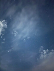 starry night sky with scattered clouds over a deep blue horizon