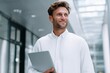 © Iftikhar alam - Office worker in white shirt smiles while holding laptop in modern business setting during daylight hours