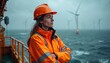 © Pete - Woman in orange safety jacket, helmet stands on platform overlooking stormy sea with offshore wind turbines. Pro engineer checks wind farm infrastructure, dedicated to sustainable energy production,
